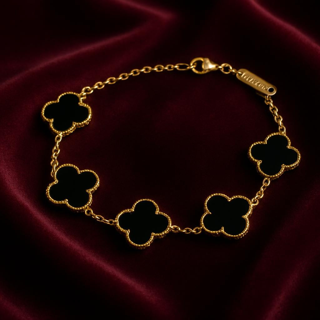 A studio shot displaying the bracelet draped over a plush velvet fabric in deep jewel tones, with a focus on the detailed craftsmanship of the gold-plated edges and black clover charms, illuminated by a spotlight to enhance the jewelry's luxurious appeal.