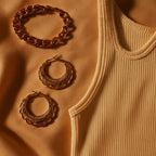 A fashionable flat lay featuring the earrings alongside complementary accessories like a gold bracelet and a chic outfit, with warm lighting that enhances the glossy shine and golden glow of the jewelry.