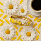 A styled flat lay featuring the gold-tone bracelet surrounded by fresh white flowers, yellow petals, and a cup of coffee, emphasizing the bright, cheerful colors and intricate details of the bangle.