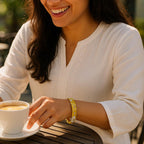 A lifestyle scene of a woman wearing the bangle with a white kurta, sitting outdoors at a sunny café table, capturing the joyful moment as she reaches for her coffee, with sunlight reflecting off the crystals.