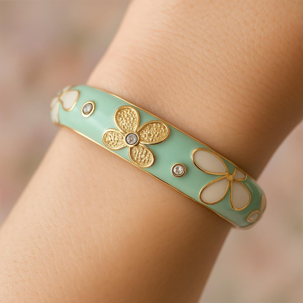 A close-up of the mint green floral enamel hinged bangle on a woman's wrist, with soft natural lighting highlighting the gold-tone flowers and scattered crystals, against a blurred pastel background.