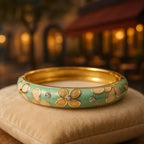 The bangle displayed on a luxurious, textured velvet cushion with a soft-focus background of a romantic café setting, emphasizing its elegance and intricate details.