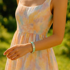 A lifestyle shot of a woman wearing the bangle paired with a pastel summer dress, walking through a sunlit garden, with the bracelet catching the sunlight and showcasing its high-gloss enamel finish.